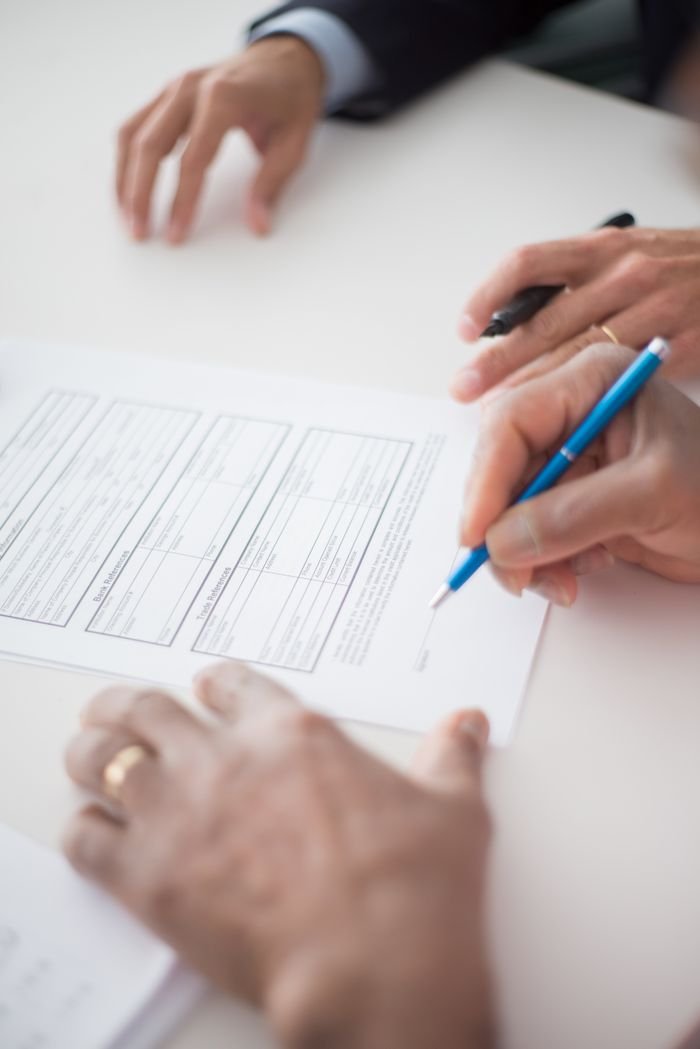 Close-up of hands signing a business document on a white surface with a pen.